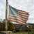Worn and tattered American flag on wooden pole with rural barn in background